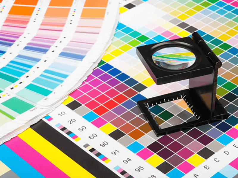 แว่นขยายสีดำวางบนชาร์ตตัวอย่างสีสดใสในงานพิมพ์อิงค์เจ็ท
