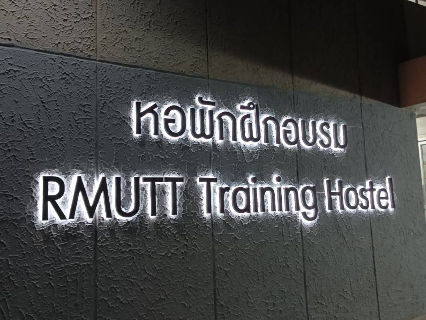 ป้ายบริษัทไฟออกหลัง RMUTT Training Hostel สีขาวส่องสว่างบนผนังลายนูน