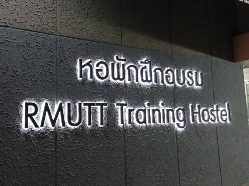 ป้ายบริษัทไฟออกหลัง RMUTT Training Hostel สีขาวส่องสว่างบนผนังลายนูน