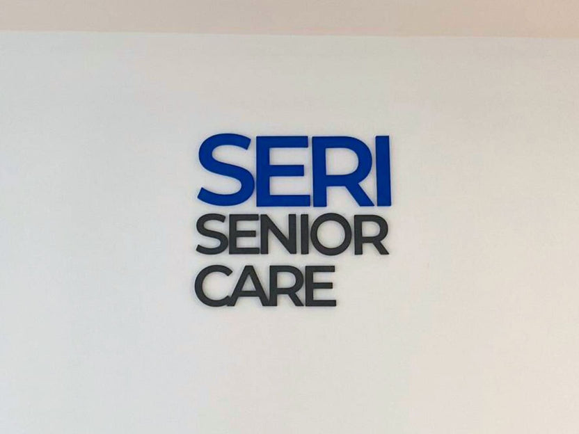 ป้ายไดคัทอะคริลิคตัวนูนสีน้ำเงินดำ Seri Senior Care บนผนังขาว