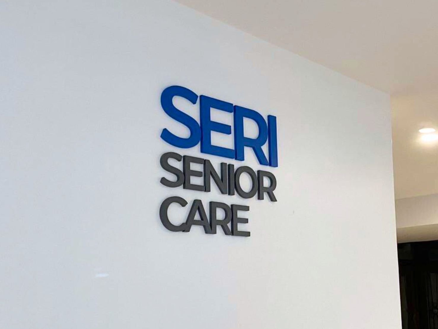 ป้ายไดคัทอะคริลิคตัวนูน Seri Senior Care สีน้ำเงินเทา 3D บนผนังขาว