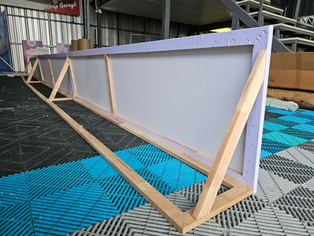 ป้ายไวนิลขึงโครงไม้ยาวสีขาวบนกรอบไม้อ่อน