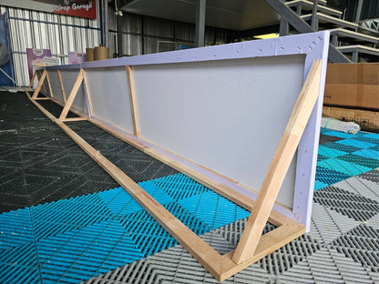 ป้ายไวนิลขึงโครงไม้ยาวสีขาวบนกรอบไม้อ่อน