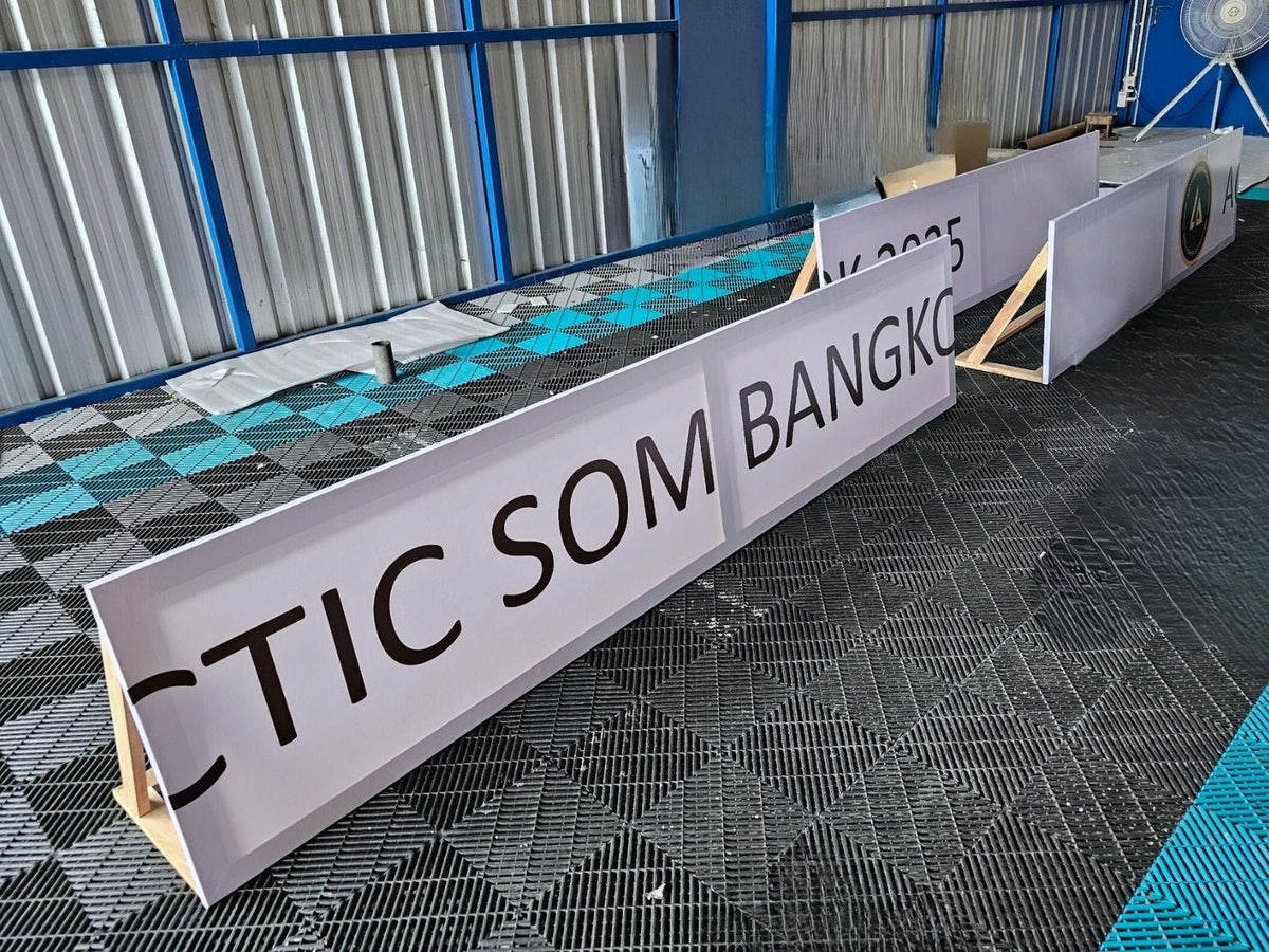 ป้ายไวนิลขึงโครงไม้ สีขาวตัวอักษรดำ ติ๊กซอมแบงค็อก บนพื้นตะแกรงเหล็ก