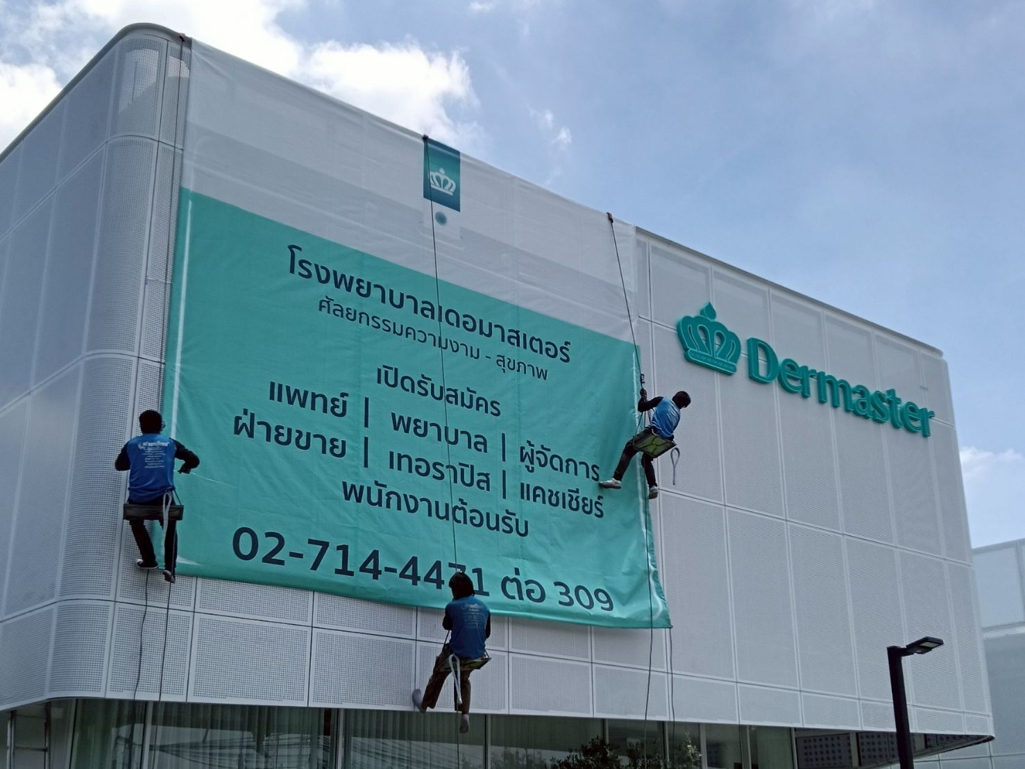 ป้ายไวนิลตาข่าย สีฟ้าเขียว พิมพ์ข้อความไทยและโลโก้ Dermaster