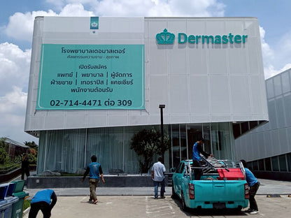 ป้ายไวนิลตาข่าย Dermaster อาคารขาวตัวอักษรฟ้าธงคราวน์