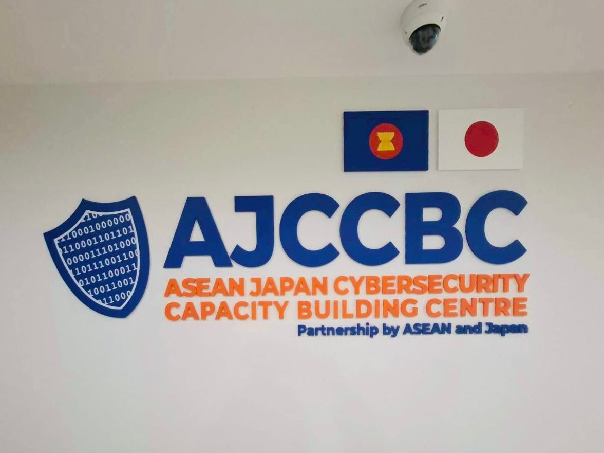 โลโก้ AJCCBC ตัวอักษร 3D สีน้ำเงินส้ม พื้นที่โล่โค้ดไบนารี่ ป้ายอะคริลิคชื่อบริษัทติดผนัง