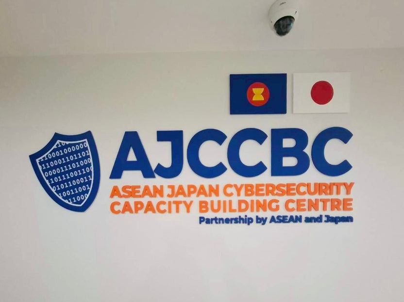 โลโก้ AJCCBC ตัวอักษร 3D สีน้ำเงินส้ม พื้นที่โล่โค้ดไบนารี่ ป้ายอะคริลิคชื่อบริษัทติดผนัง