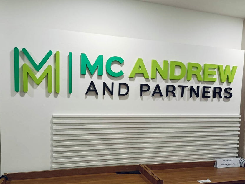 ป้ายพลาสวูดตัวนูน 3 มิติ สีเขียวดำ Mc Andrew and Partners บนผนังขาว