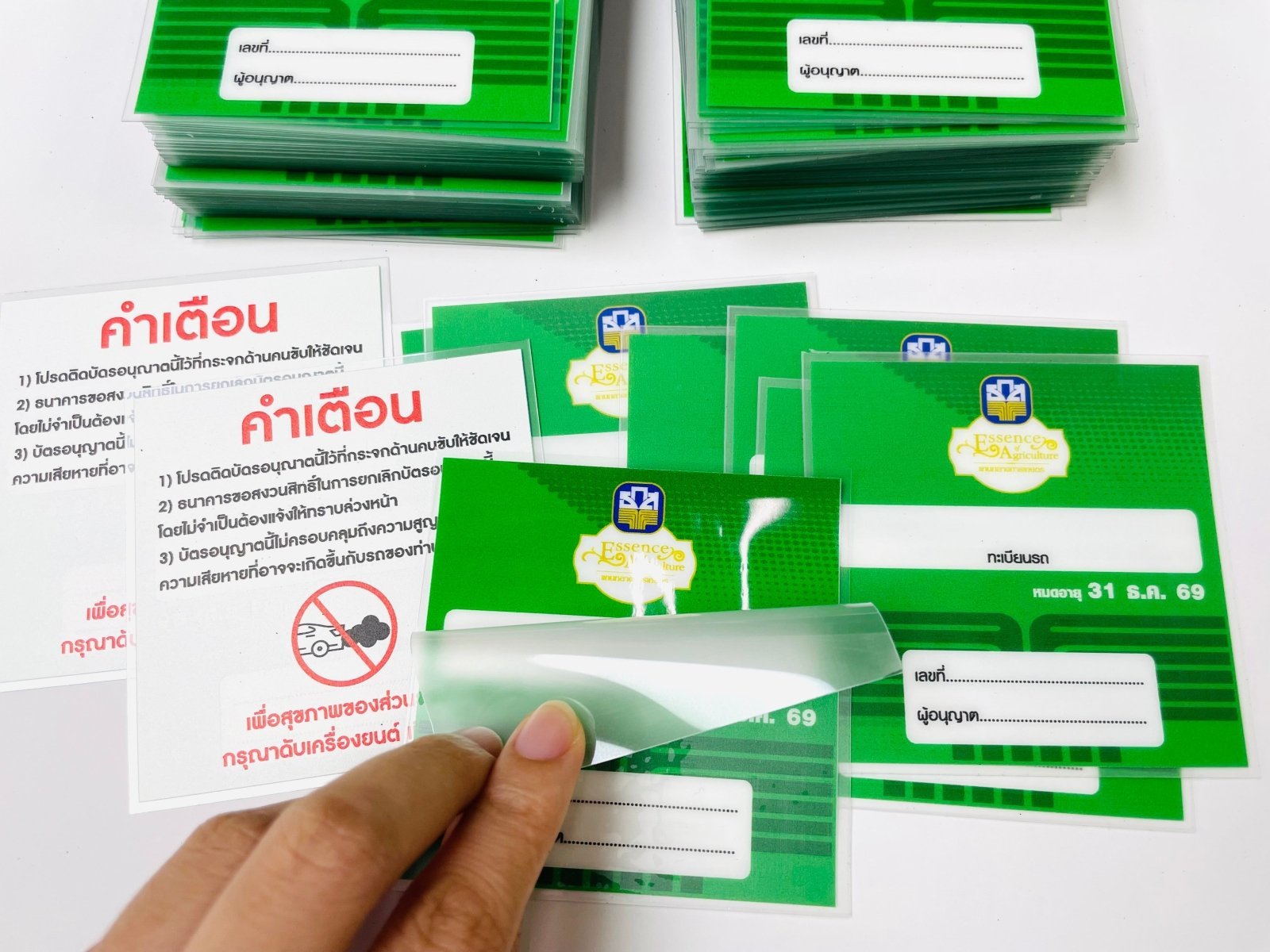 บัตรไอดีพลาสติกสีเขียวมีฉลากขาวและตราสีน้ำเงิน ในซองใสป้องกัน