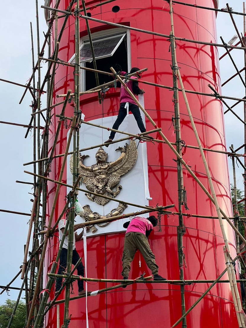 ติดตั้งตราประดับการุฑทองบนหอคอยทรงกระบอกสีแดง